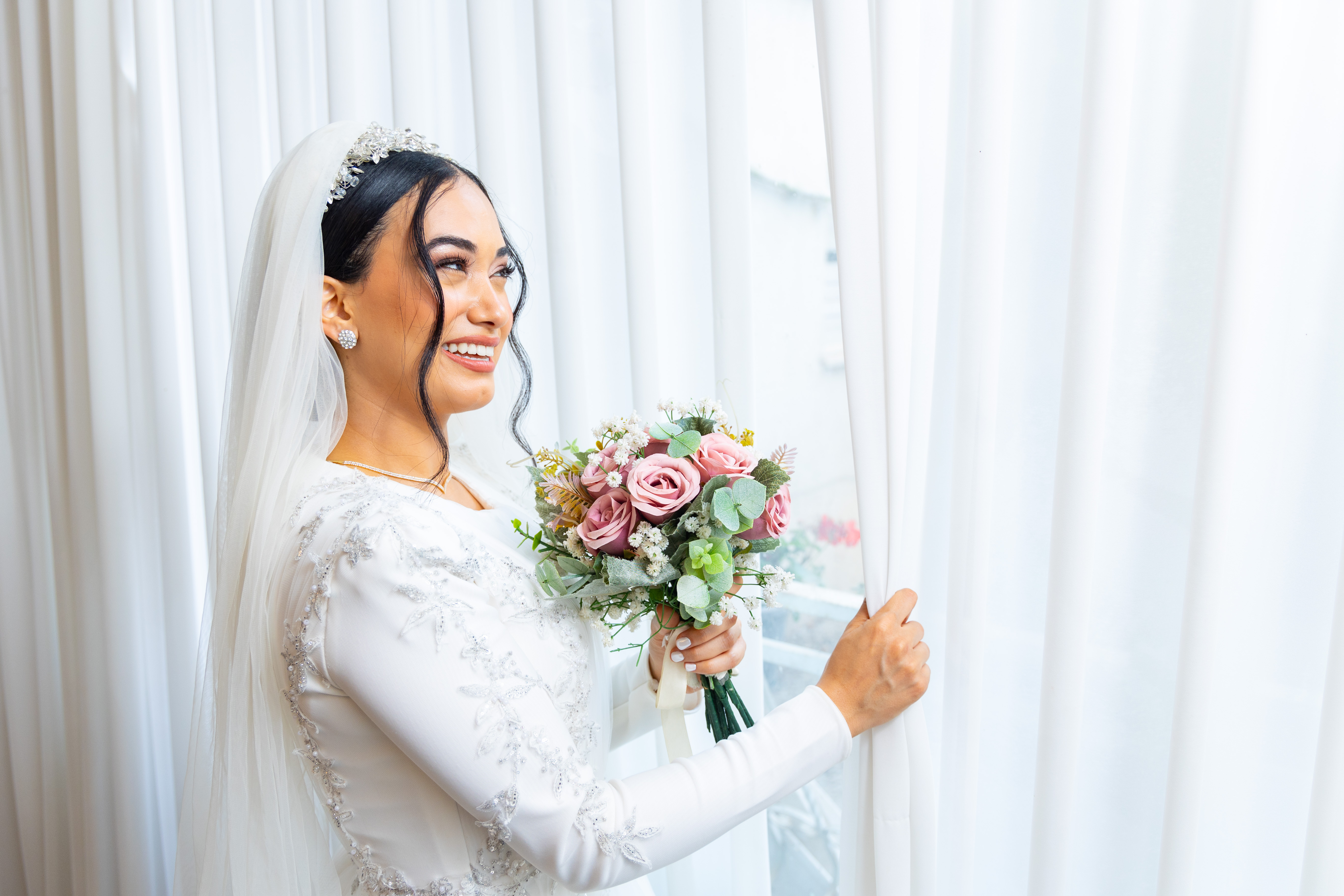 A bride with her bouquet beside a window